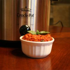 a white bowl filled with food sitting on top of a wooden table next to an electric crock pot