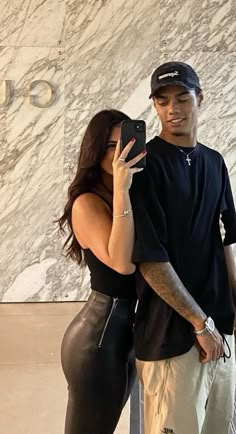 a man and woman taking a selfie in front of a marble wall with their cell phones