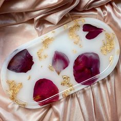 a white plate topped with red flowers and gold flakes on top of a pink satin