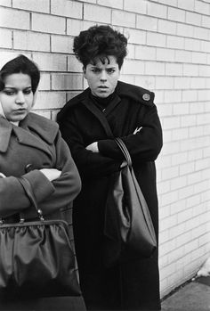 two women standing next to each other in front of a brick wall