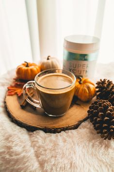 a cup of coffee sitting on top of a wooden tray next to some pine cones