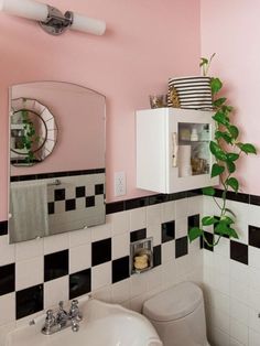 a bathroom with pink walls and black and white tiles on the wall, mirror above the sink