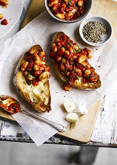 two pieces of bread with beans and sauces on them sitting on a cutting board