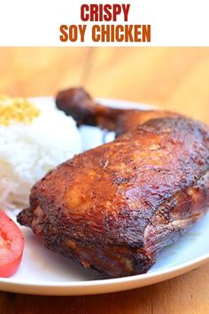 a white plate topped with meat and rice next to a slice of tomato on top of a wooden table