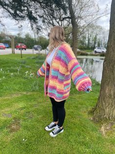 a woman standing next to a tree wearing a colorful crocheted cardigan sweater