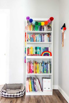 a white book shelf filled with lots of books next to a dog bed on top of a hard wood floor