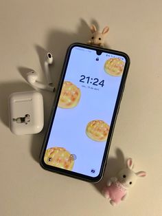 an iphone is next to a small toy rabbit and ear buds on a table top