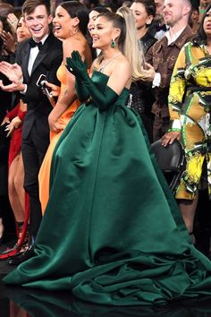 two women in green dresses standing next to each other and people behind them looking at the camera