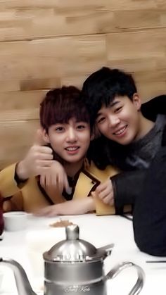 two young men posing for a photo in front of a teapot and kettle on a table