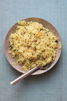 a bowl filled with rice and vegetables on top of a blue table cloth next to a spoon