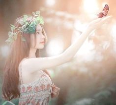 a woman holding a butterfly in her hand and wearing a flower crown on her head