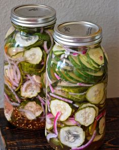 two mason jars filled with pickles, onions and cucumbers on a table