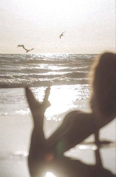 a woman standing on top of a beach next to the ocean with birds flying overhead