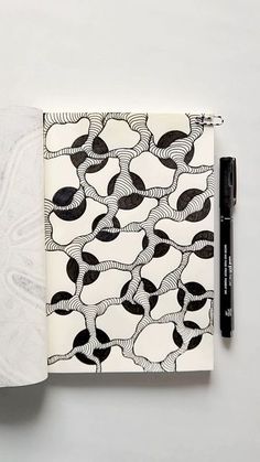 an open notebook with black and white designs on it, next to a marker pen