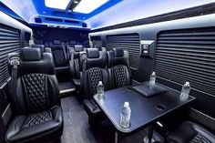 the interior of a bus with black leather seats and tables, bottles of water on each side