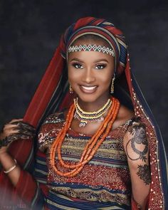 a woman in an ethnic dress and headdress with tattoos on her arms, smiling at the camera