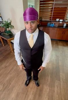 a man in a suit and tie standing on a hard wood floor wearing a purple turban