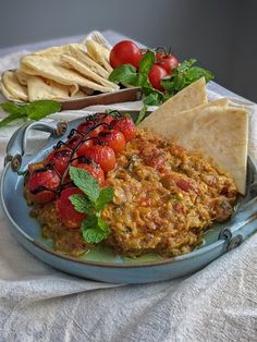 a blue plate topped with food next to tortilla chips and tomato salad on top of a white table cloth