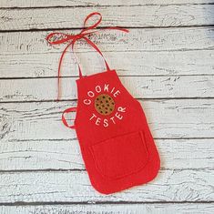 an oven mitt with a cookie on it is hanging from a string and sits on a white wooden surface