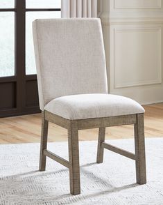 a white chair sitting on top of a rug in front of a window with curtains