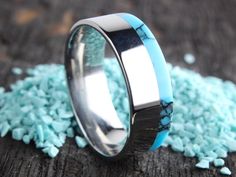 a wedding ring with blue and silver inlays on top of some turquoise gravel