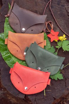 three leather purses sitting on top of a leafy green tree stump with leaves around them