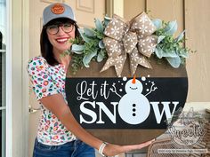 a woman standing next to a sign that says let it snow with a snowman on it