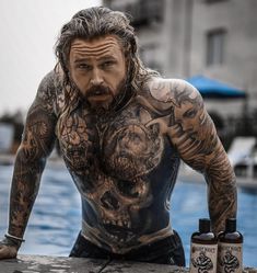 a man with tattoos sitting next to a pool