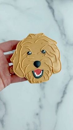 a hand holding a cookie with a dog's face on it, and the cookie is shaped like a golden retriever