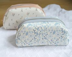 two small cosmetic bags sitting on top of a white towel next to eachother