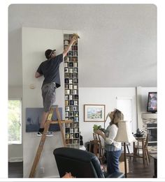 a man and woman are standing on a ladder in the middle of a living room