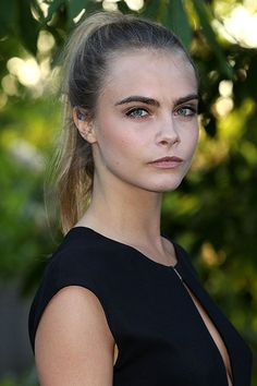 a young woman in a black dress is posing for the camera with her hair pulled back