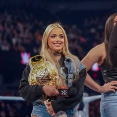 the beautiful blonde woman is holding her wwe championship belt and smiling at the camera while standing in front of two other women