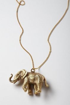 an elephant necklace is shown on a white surface with a gold colored chain and it's head turned to the side