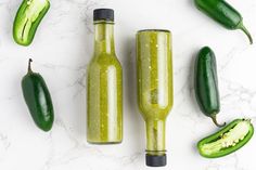 three bottles filled with green liquid next to cucumbers on a marble counter top