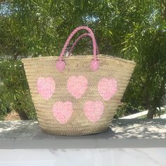 Our large hand woven straw tote with pink sequin hearts is such a sweet addition to the collection! It's made by hand with wicker palm straw that is sourced locally in Morocco. One side has hand sewn pink sequins in the shape of hearts and the other side is plain straw. Handcrafted in Morocco Straw with leather handles Individually hand sewn pink sequins 22"W x 13" H x 7.5"D (interior capacity - large) 7" strap drop Draw string liner that closes at the top of bag to secure your belongings Sustai Pink Handwoven Straw Bag For Summer, Pink Straw Bag For Summer Shopping, Handmade Pink Straw Tote Bag, Handmade Pink Bucket Straw Bag, Pink Straw Shopping Bag, Pink Handwoven Straw Bag, Pink Straw Bag With Braided Handles, Luxury Pink Straw Shopping Bag, Pink Handwoven Bucket Straw Bag