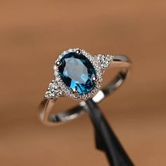 It is a London blue topaz ring. The main stone is 6mm*8mm oval cut, weight about 1.47carats. The basic metal is sterling silver and plated with rhodium.  To change the metal to a solid gold (white/rose) or platinum is also available, please ask for a quotation if you want.  You can also go to my shop Home for more elegant rings: https://www.etsy.com/shop/godjewelry?ref=hdr_shop_menu  More rings: https://www.etsy.com/shop/godjewelry?ref=l2... Formal Oval Topaz Ring With Halo Setting, Dazzling Oval Topaz Ring, Oval Birthstone Promise Ring In 14k White Gold, Oval Birthstone Ring In 14k White Gold For Promise, Oval Cubic Zirconia Topaz Ring Birthstone, Oval Cubic Zirconia Topaz Birthstone Ring, Anniversary Oval Blue Topaz Diamond Ring, Silver Oval Topaz Ring For Anniversary, Classic Halo Topaz Ring For Wedding