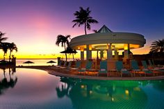 an outdoor swimming pool with chaise lounges and palm trees in the background at sunset