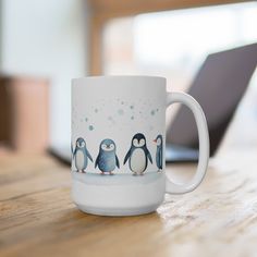 a white coffee mug with penguins on it sitting on a table next to a laptop