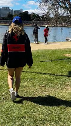 a woman walking across a lush green field next to a lake