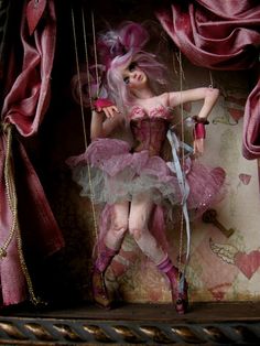 a doll with pink hair is sitting on a swing in front of a red curtain