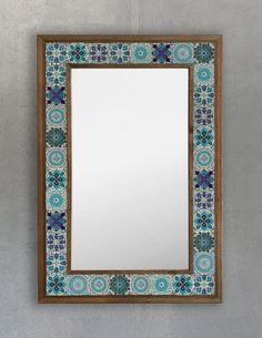 a mirror hanging on the side of a wall with blue and green flowers in it