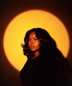 a woman standing in front of a yellow sun with her shadow on the wall behind her