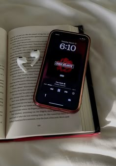 an open book with earbuds laying next to it on top of a bed