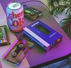 a table topped with cassettes and a can of cheer cola next to an mp3 player