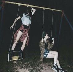 two young women sitting on swings in the dark, one is holding her leg up