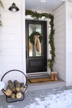 the front door is decorated for christmas with wreaths and firewood on the porch