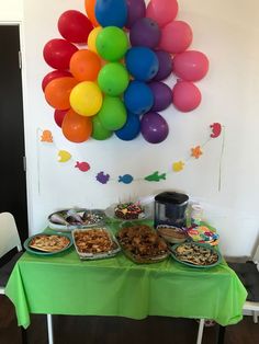 a table topped with lots of food next to a colorful balloon wall hanging on the wall