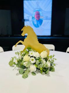 a white table topped with a vase filled with flowers and a golden horse decoration on top of it