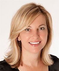 a woman with blonde hair wearing a black shirt and smiling at the camera while standing in front of a white background